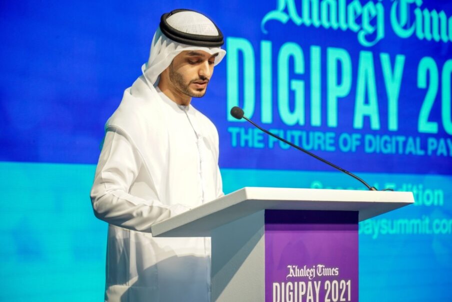 A man in traditional Middle Eastern attire speaks at a podium at an event labeled