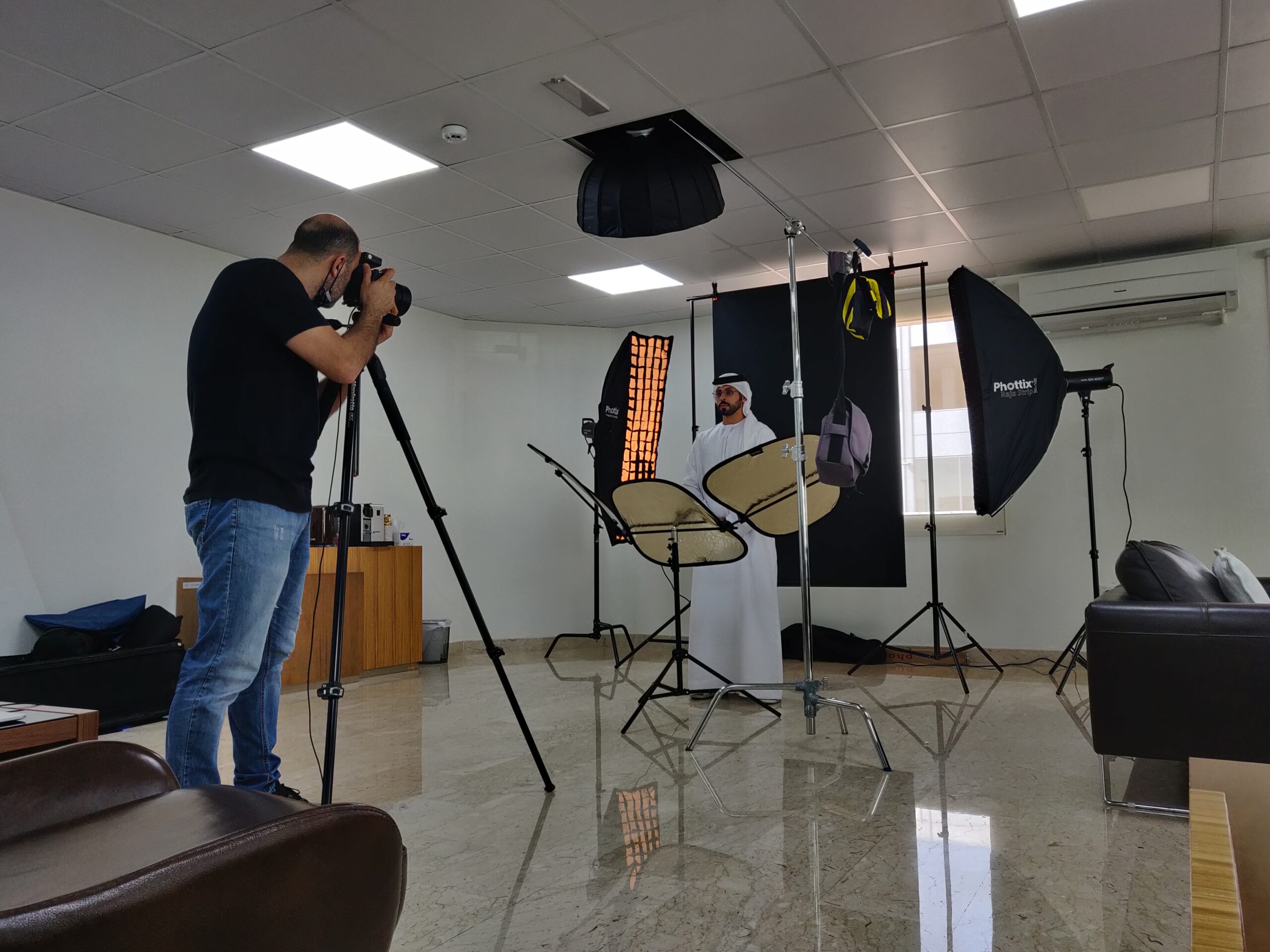 Two people are standing in front of a green screen with professional lighting and a reflector disc around them.