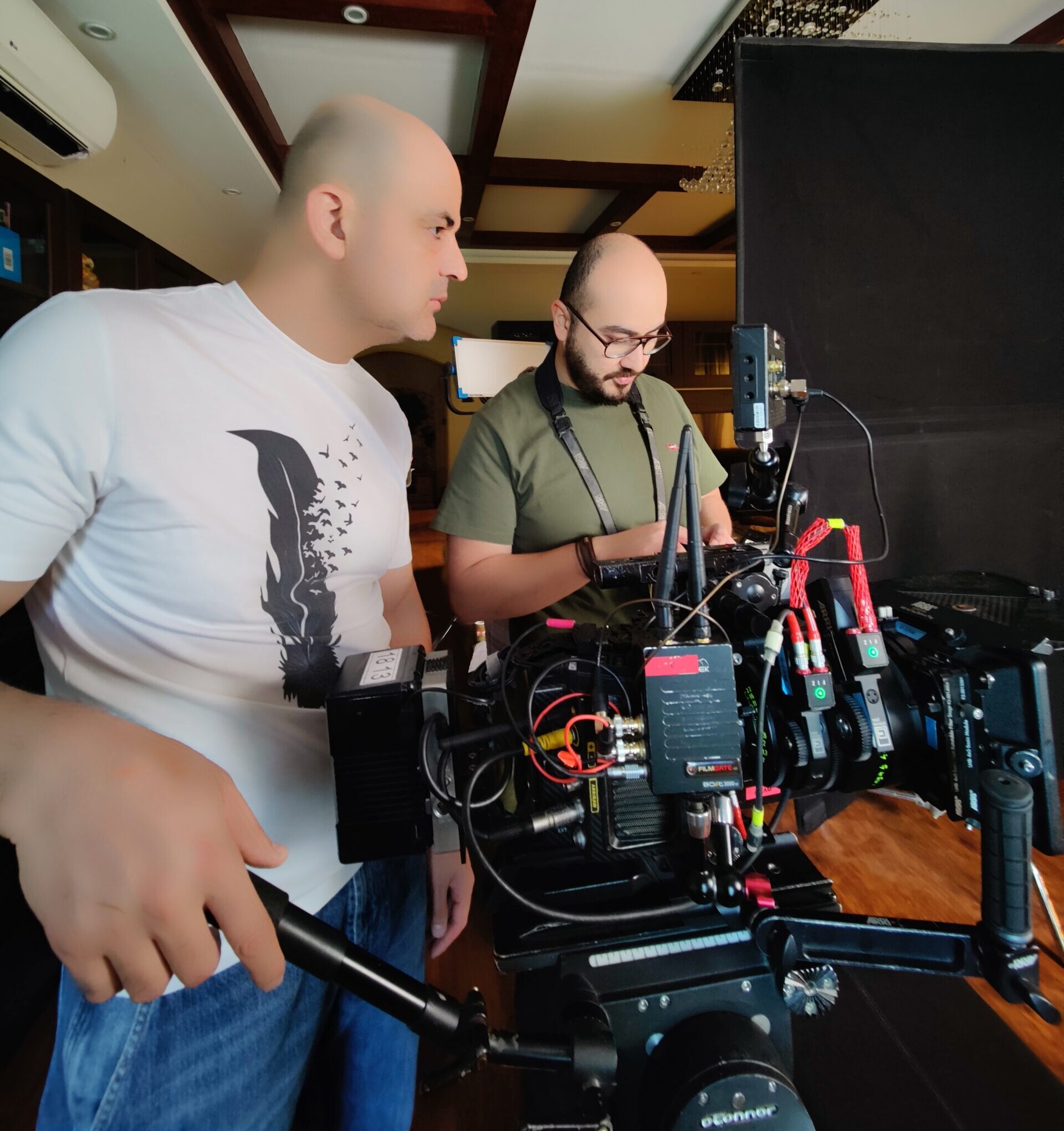 A man in suit sits at conference table with documents, office equipment and video recording setup are arranged around him.